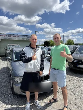 Dwóch klientów z kciukiem w górę przy ciemnym sedanie