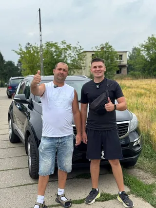 Dwóch klientów przy ciemnym aucie, w tle pole