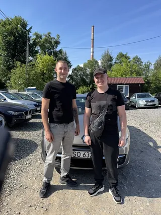 Dwóch klientów przy ciemnym aucie na żwirowym placu